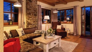 A cozy living room with a stone wall, wooden ceiling, a brown leather sofa, a white coffee table, and a red bag.