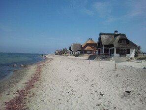 Uma praia com casas de palha, areia dourada e céu azul límpido.