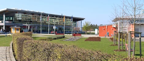 A modern building with a glass facade, a well-maintained garden with benches, and a clear sky.