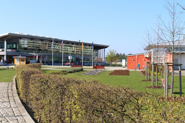 Um edifício moderno com fachada de vidro, um jardim bem cuidado com bancos e um céu limpo.
