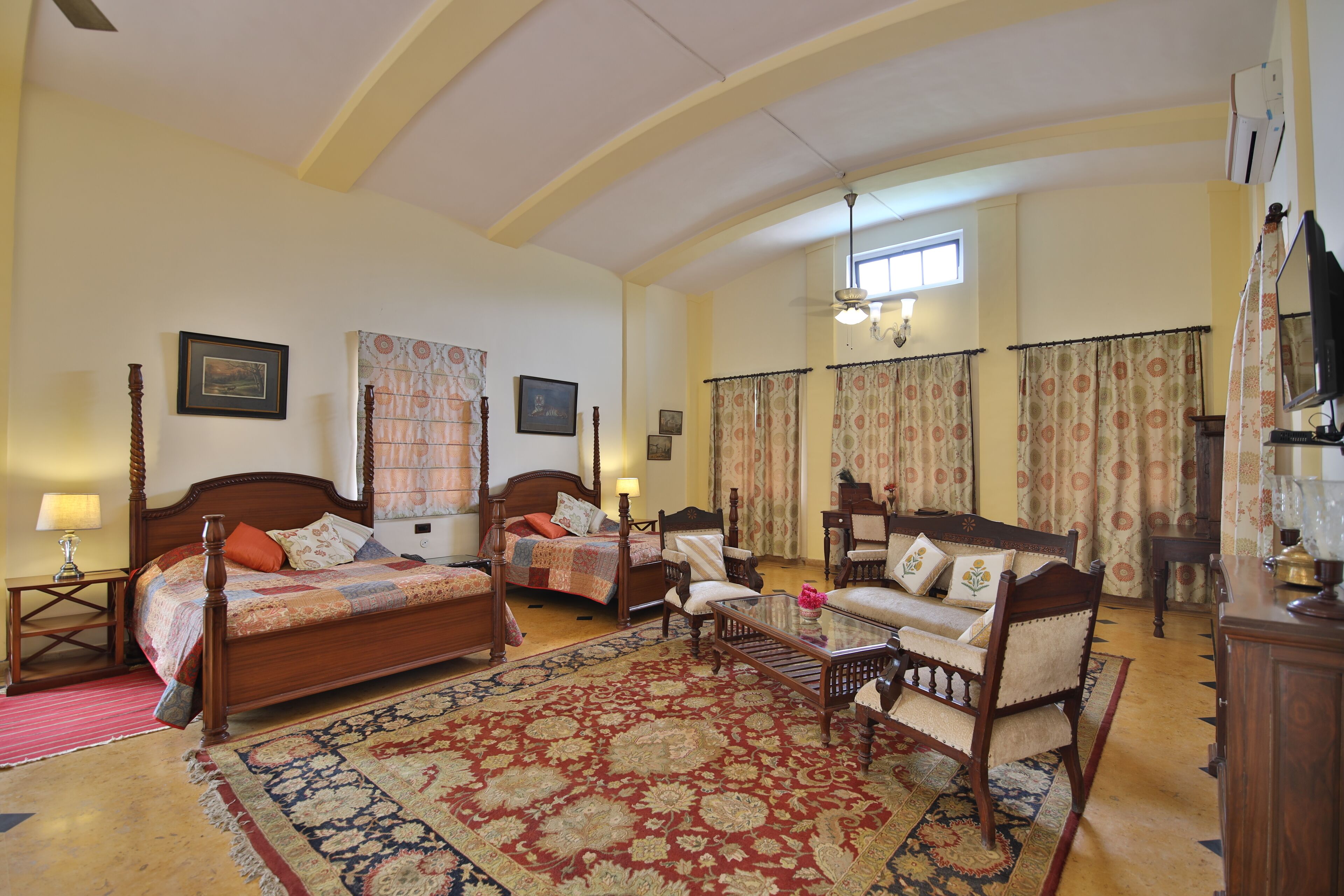 A spacious bedroom with two beds, a sitting area with a sofa and armchairs, and a large ornate rug.