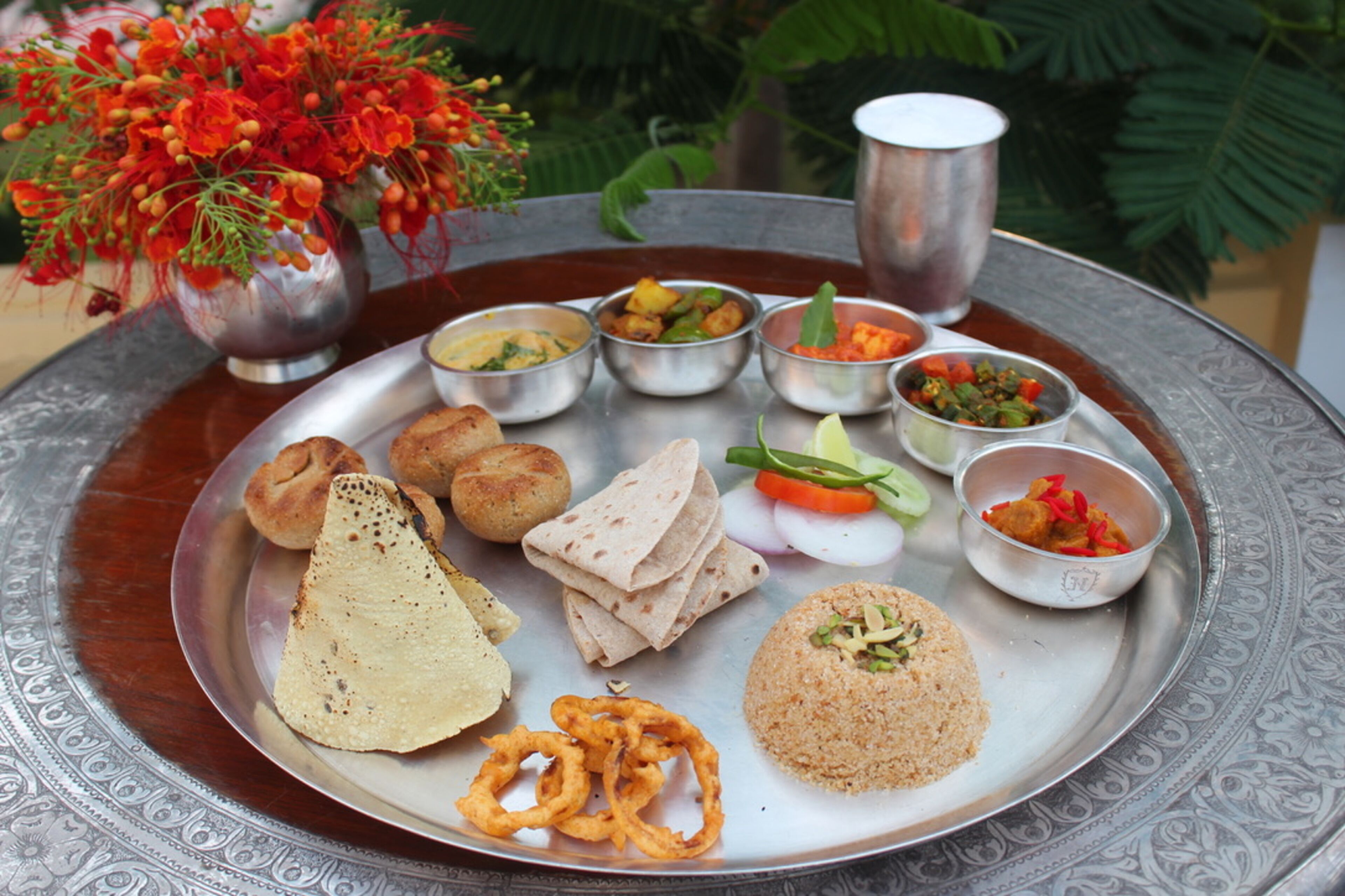 A traditional Indian meal on a metal tray with various dishes, including flatbreads, curries, and rice.