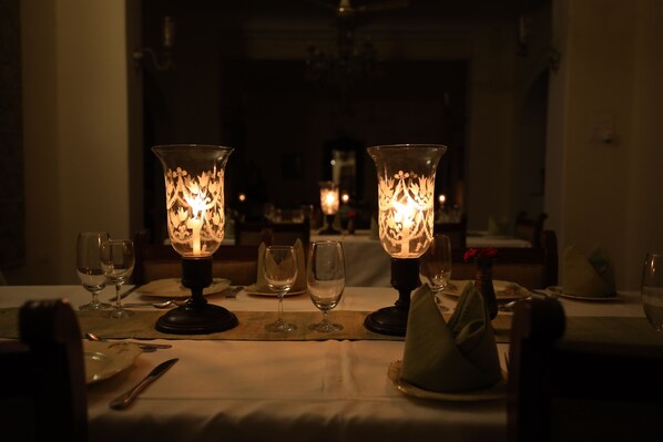A dimly lit dining area with two ornate table lamps, wine glasses, and a table set for two. - Roop Niwas Kothi (Nawalgarh)