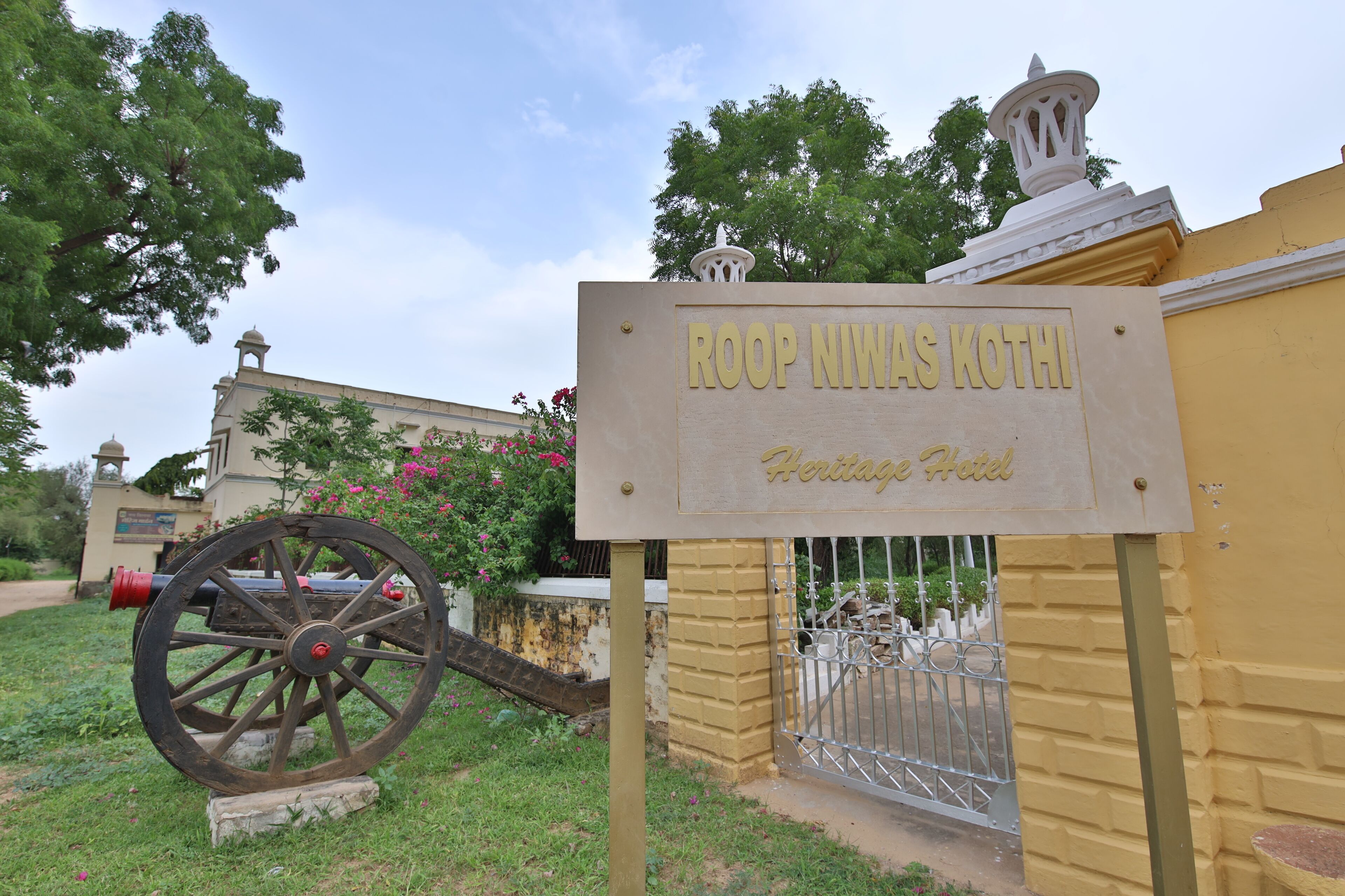 A sign for Roop Niwas Kothi Heritage Hotel with a large cannon in the foreground.