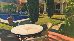 Un espace aménagé au bord de la piscine, avec une table ronde et des chaises, une piscine, et un bâtiment doté d’un balcon en arrière-plan.
