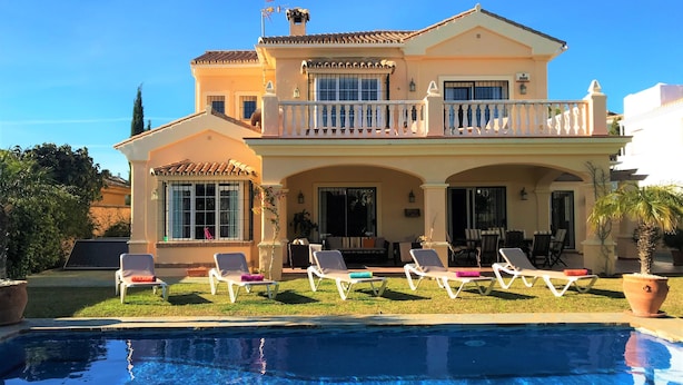 Une maison à deux étages avec une piscine, un espace salon extérieur et un grand balcon.