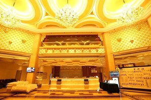 A hotel lobby with a reception desk, seating area, and decorative chandeliers. - Victoria Hotels (Foshan)