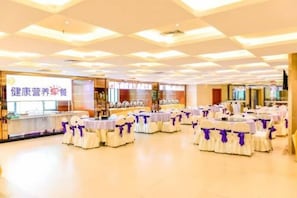 A banquet hall with round tables covered in white tablecloths and purple sashes, arranged in rows.