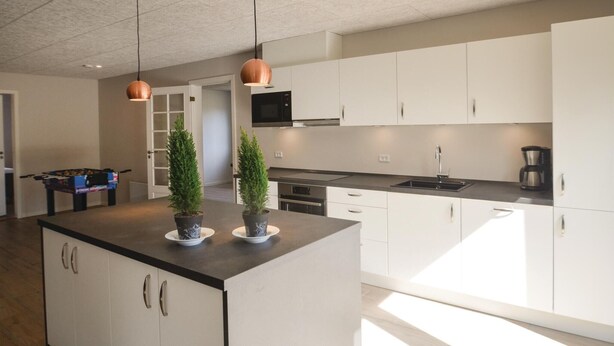 Une cuisine moderne avec des meubles blancs, un plan de travail noir et deux suspensions lumineuses.
