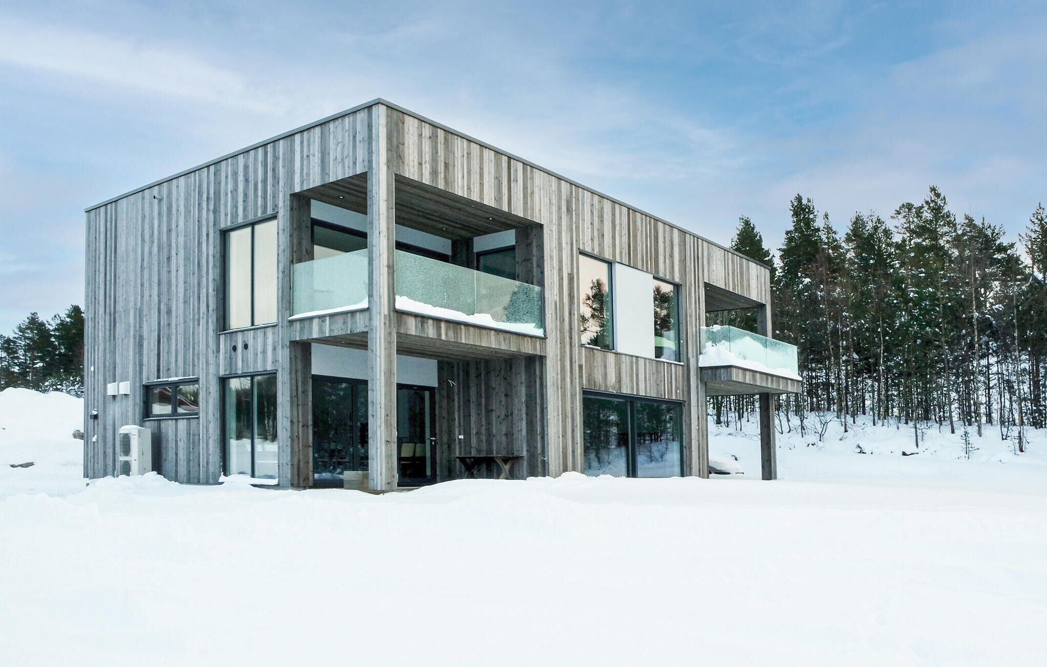 A modern, multi-story building with large windows and a balcony, surrounded by snow and trees.