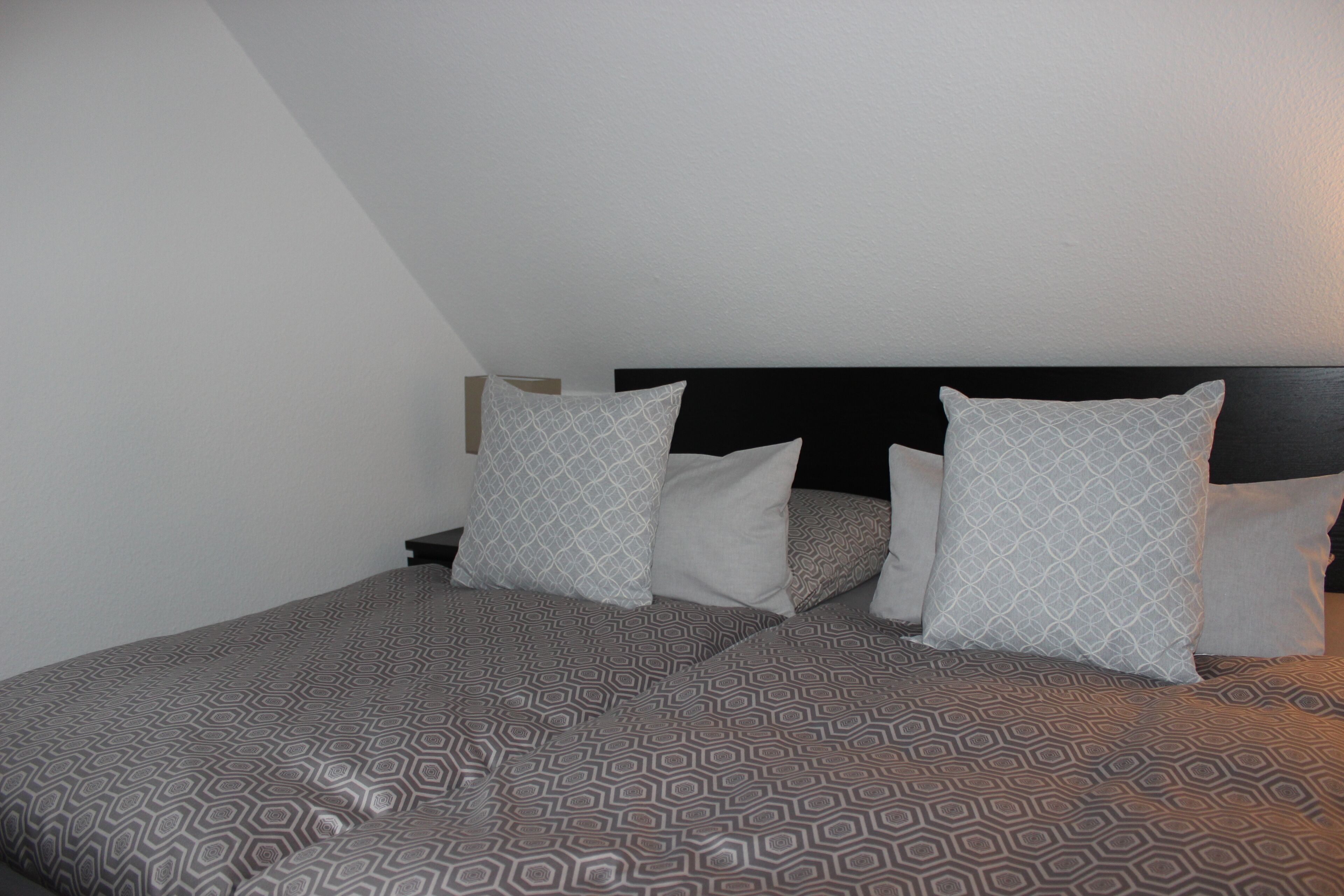 Une chambre à coucher avec une couvre-lit à motifs, une tête de lit noire et trois coussins au motif géométrique.