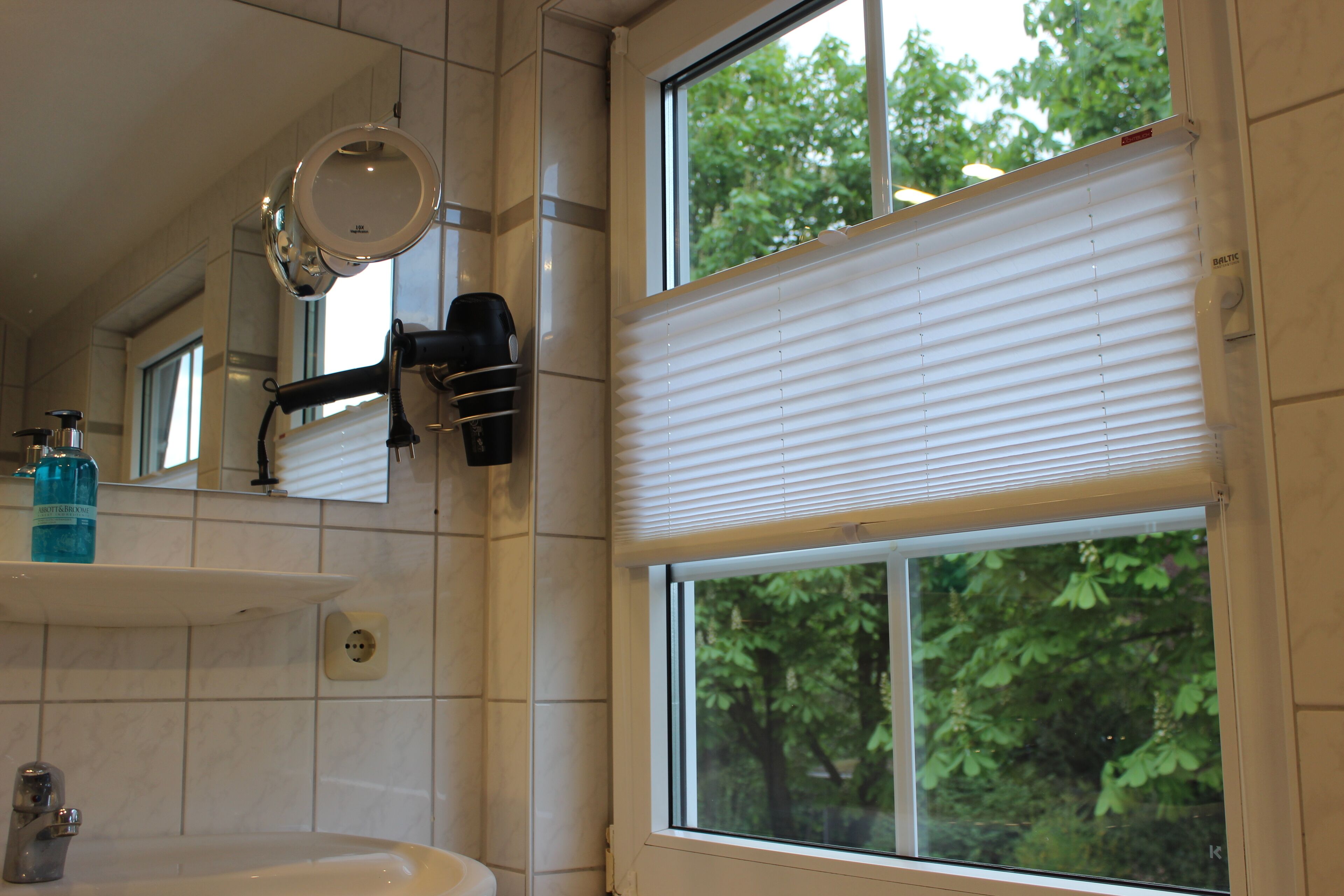Een badkamer met een wastafel, spiegel en raam met jaloezieën.