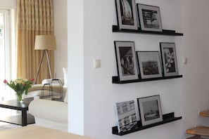 A living room with a sofa, a coffee table with a vase of flowers, a floor lamp, and a wall with framed pictures. - Semi-detached house on the border to Hamburg between "Old Land" and Nordheide (Neu Wulmstorf/Rade)