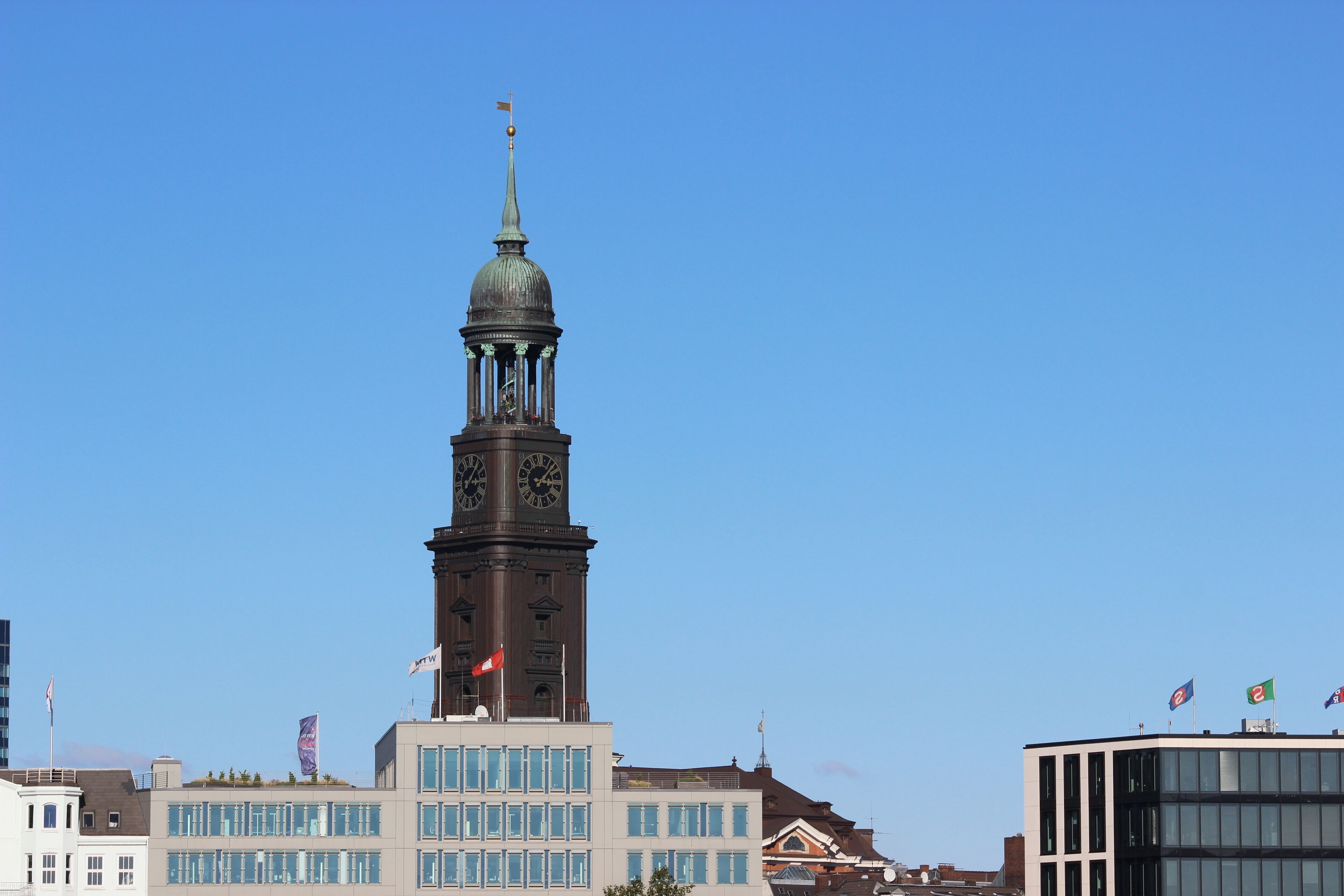 Ein historisches Gebäude mit einem Uhrturm, modernen Glasfenstern und Flaggen.