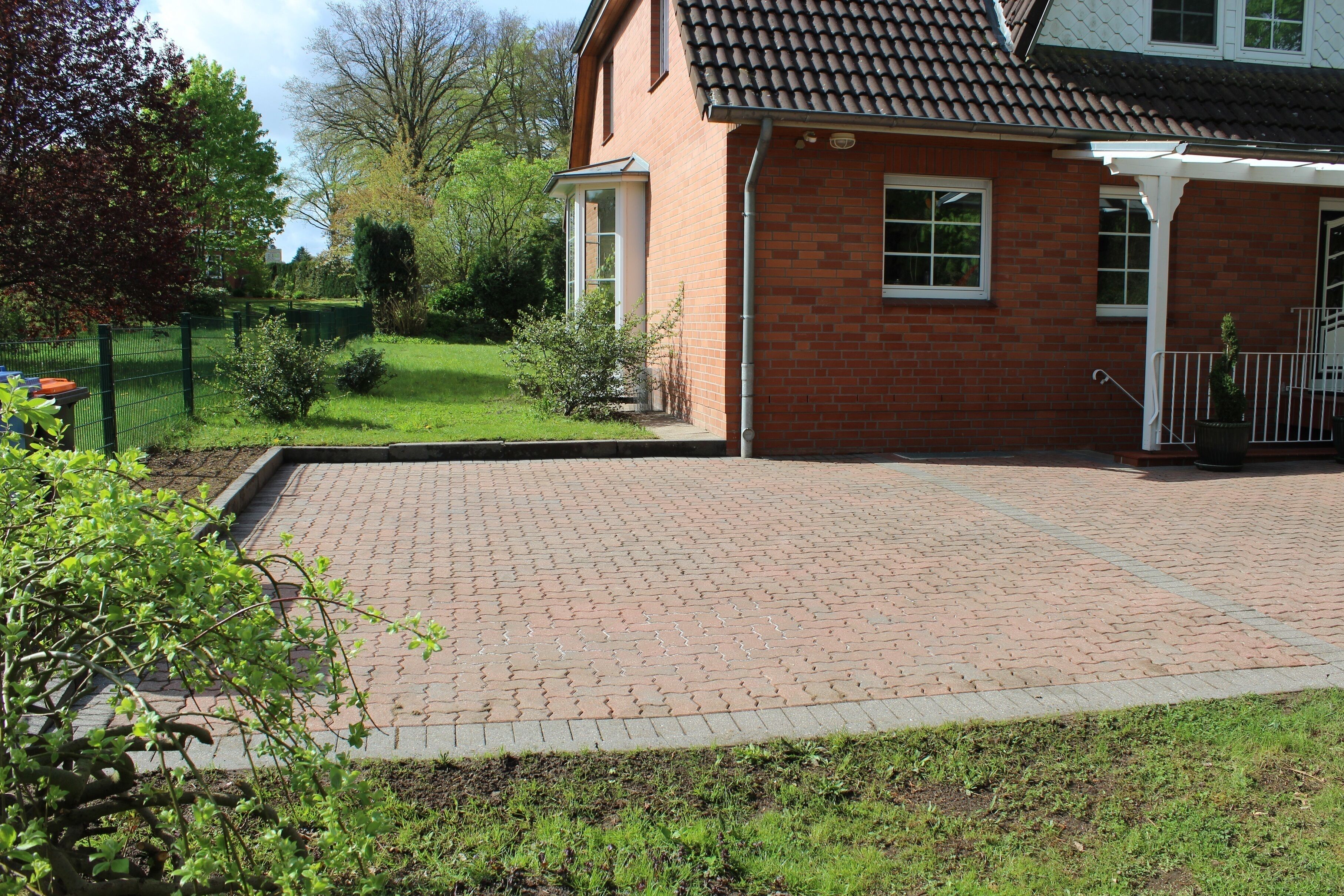 Een bakstenen huis met een betegeld terras, een omheind erf en een kleine tuin.