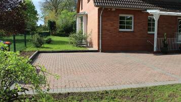 Een bakstenen huis met een betegeld terras, een omheind erf en een kleine tuin.