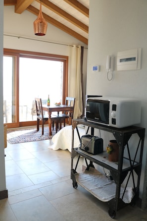 Une cuisine équipée d’un four à micro-ondes posé sur un chariot, une table à manger avec des chaises, et une vue sur un espace extérieur.