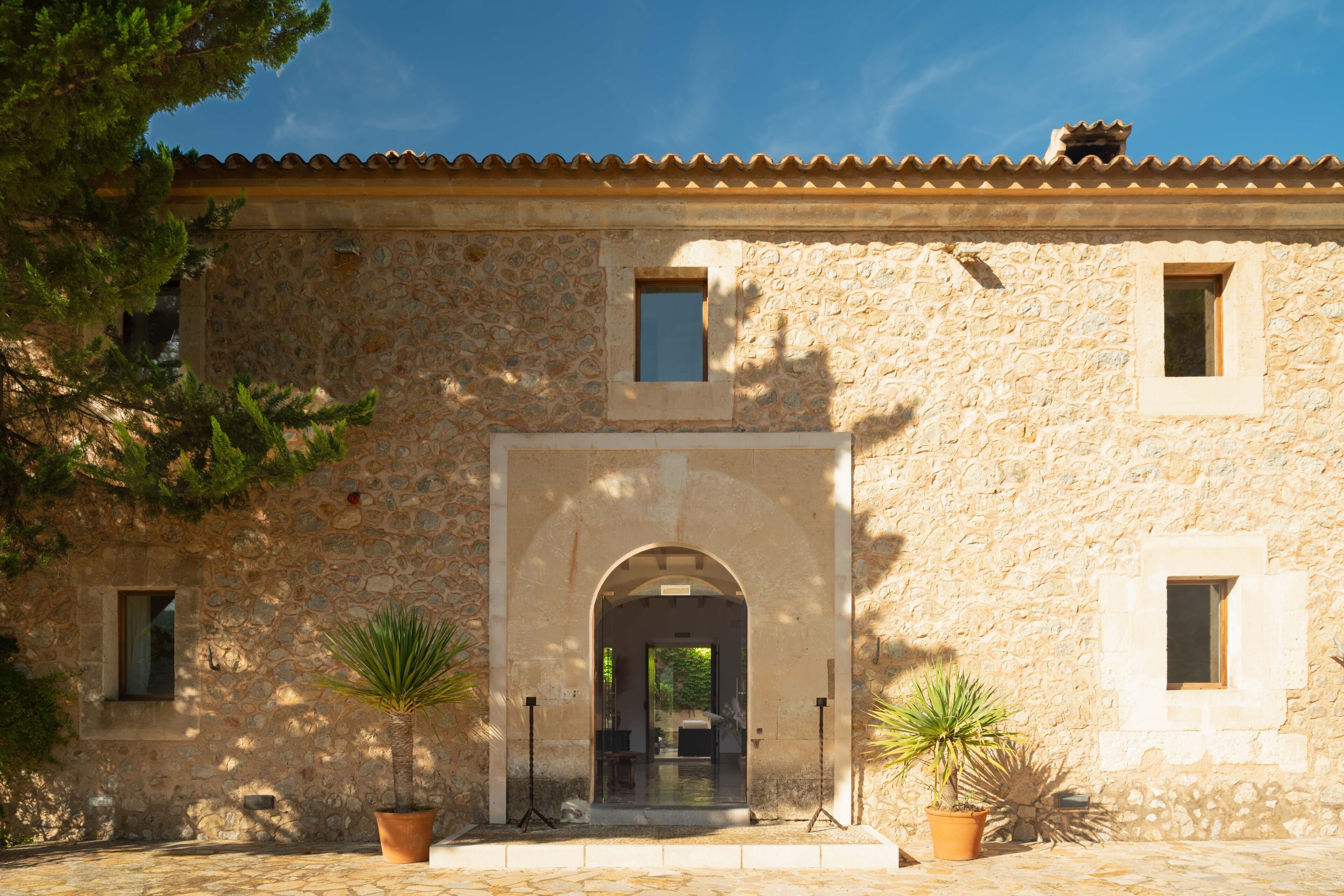 A stone building with an arched entrance, potted plants, and a tiled roof.