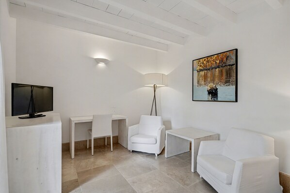 A modern, minimalist room with a flat-screen TV, a desk, two white chairs, a floor lamp, and a painting of a bridge.