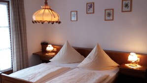 Un lit bien fait, avec deux oreillers, une lampe de chevet et une lampe fixée au mur. Quatre tableaux encadrés ornent le mur.