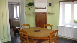 Zona pranzo con tavolo rotondo in legno e quattro sedie. Si nota una porta in legno con un piccolo oblò sopra, e uno scaffale con oggetti decorativi.