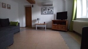 Un soggiorno con un divano scuro, un tavolino con una lampada, un mobiletto in legno e un televisore.