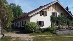 Una casa a due piani con tetto spiovente, persiane in legno e un muro in pietra.