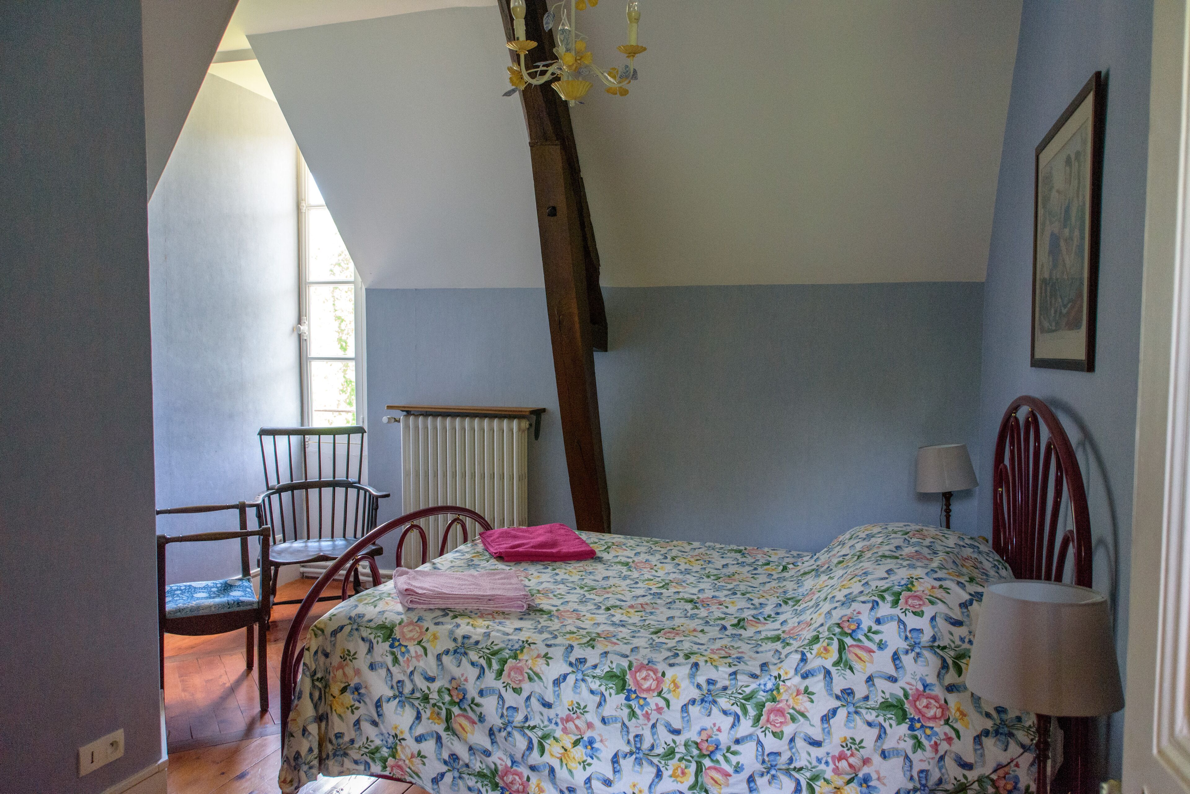 A bedroom with a bed, a chair, a radiator, and a window.