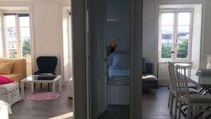 Een ruime woonkamer met een bank, een stoel, een eettafel met stoelen en een uitzicht door een geopende deur.