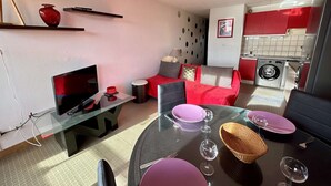 A compact living space with a sofa, a TV, a dining table set for two, and a kitchen area with a washing machine. - 2-Bedroom Apt Cabin, Parking, Pets Allowed - Cap d'Agde (Cap d'Agde)