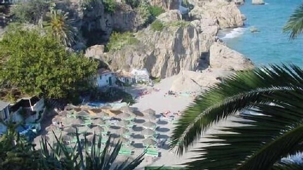 A coastal view with rocky cliffs, a beach with umbrellas, and palm trees. - Large house, ideal private heated pool for family vacation (Vélez-Málaga)