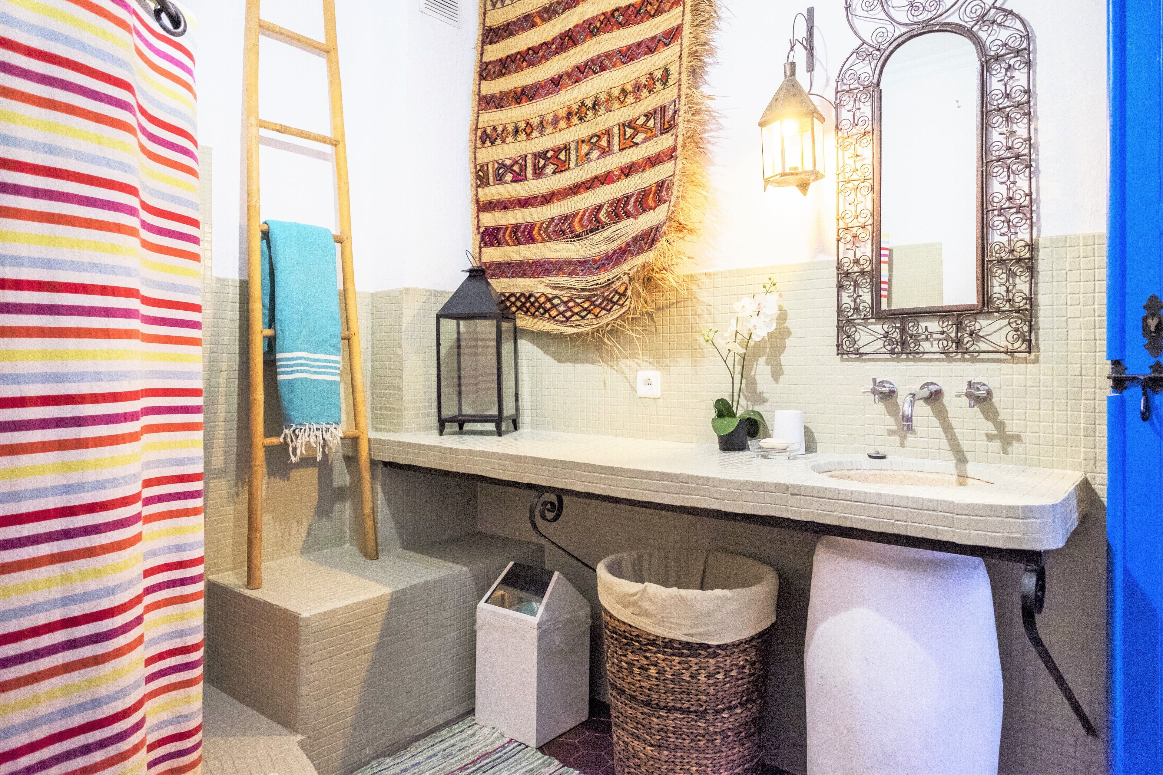A bathroom with a white sink, a mirror, a towel rack, a trash bin, and a patterned rug.