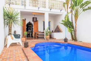 A pool area with a tiled floor, a wooden bench, and potted plants.