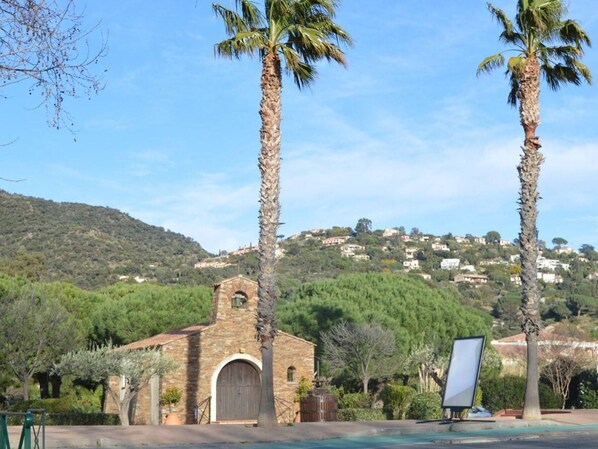 A stone building with a small arched entrance, surrounded by palm trees and a hilly landscape in the background.