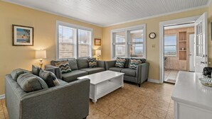 A living room with a gray sectional sofa, a white coffee table, and two windows with blinds.