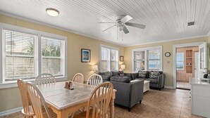 A spacious living room with a dining area, a gray sofa, wooden chairs, and a ceiling fan.
