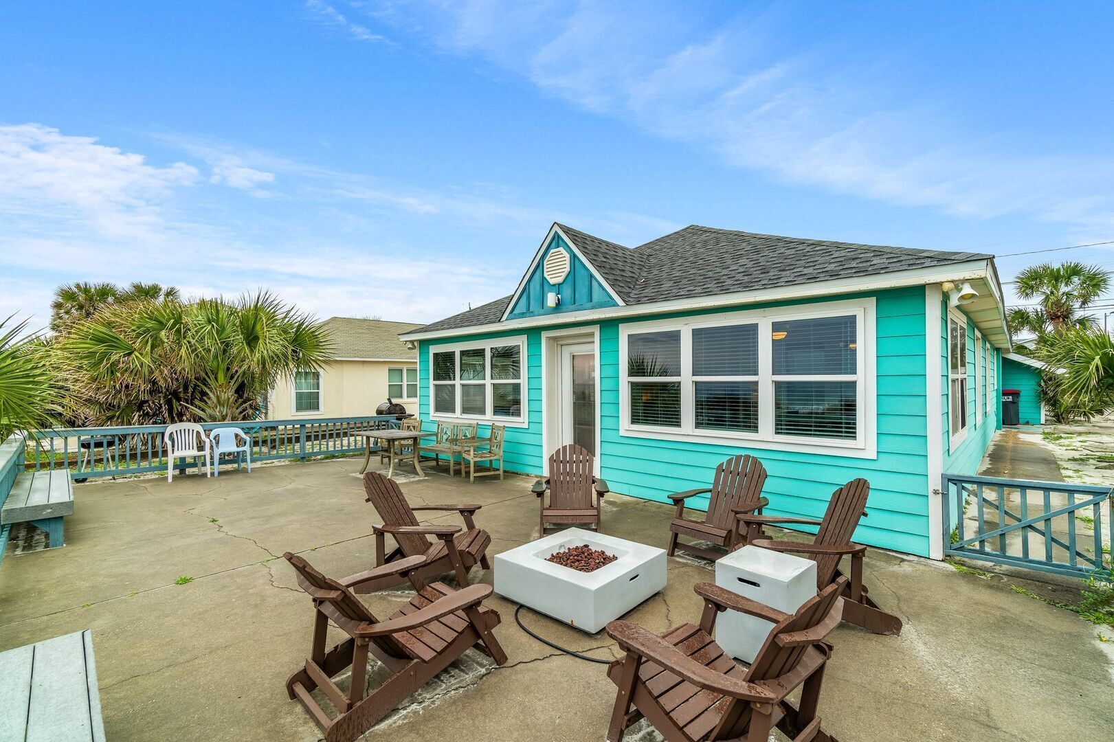 Een huis met een turquoise gevel en een overdekt terras, met houten stoelen en een tafel.