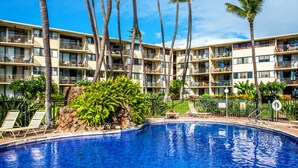 A hotel with a swimming pool surrounded by palm trees and lounge chairs.
