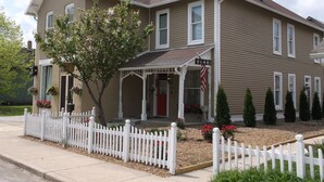 A two-story house with a porch, a picket fence, and a small garden with red flowers. - DOWNTOWN INDY HOME IN HISTORIC LOCKERBIE SQUARE  - 7 BLOCKS FROM CITY CENTER! (Indianapolis)