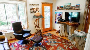 A living room with a leather sofa, a black chair, a red patterned rug, a wooden coffee table, and a television on a wooden stand. - Red rock canyon views! Private. Everything you need. Artist touches abound (Sedona)