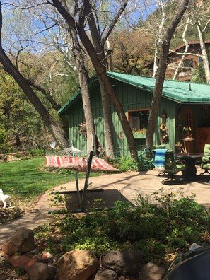 Un chalet rustique avec un toit végétalisé, entouré d’arbres et agrémenté d’un hamac.