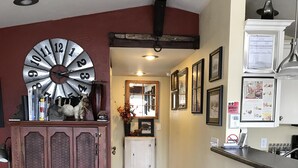 A hallway with a wooden floor, a vintage clock, a cabinet with glass doors, and a kitchen area with a refrigerator and a sink.