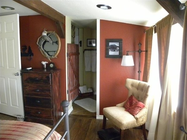 Una habitación con un aparador de madera, una silla con un cojín rojo, una lámpara y un cuadro en la pared.