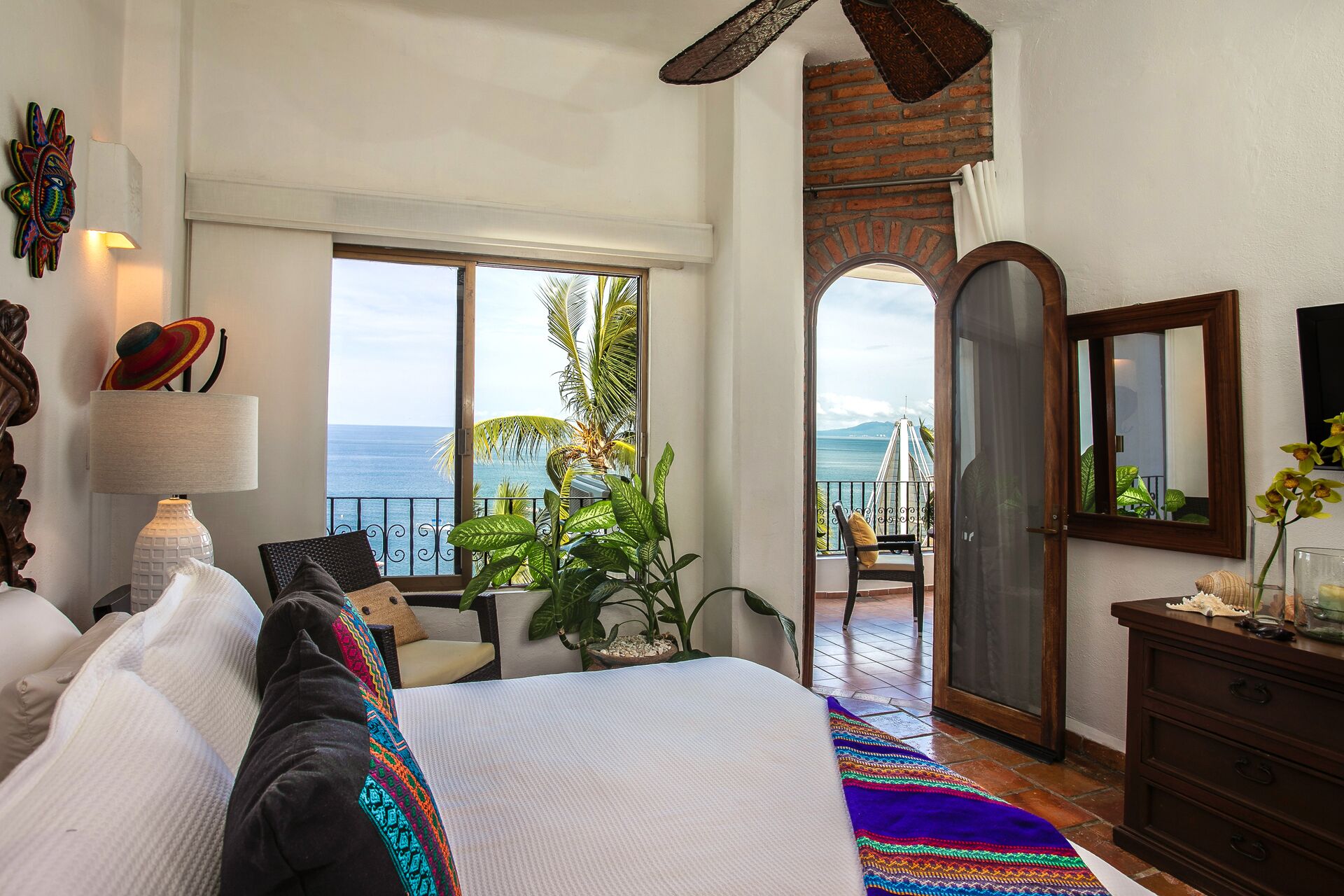 Une chambre avec un grand lit, une vue sur la mer, un balcon agrémenté de plantes et une porte en bois.
