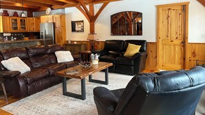 Un vaste salon doté d’un haut plafond, de poutres apparentes, d’une cheminée, d’un coin repas et d’une cuisine avec des meubles en bois.
