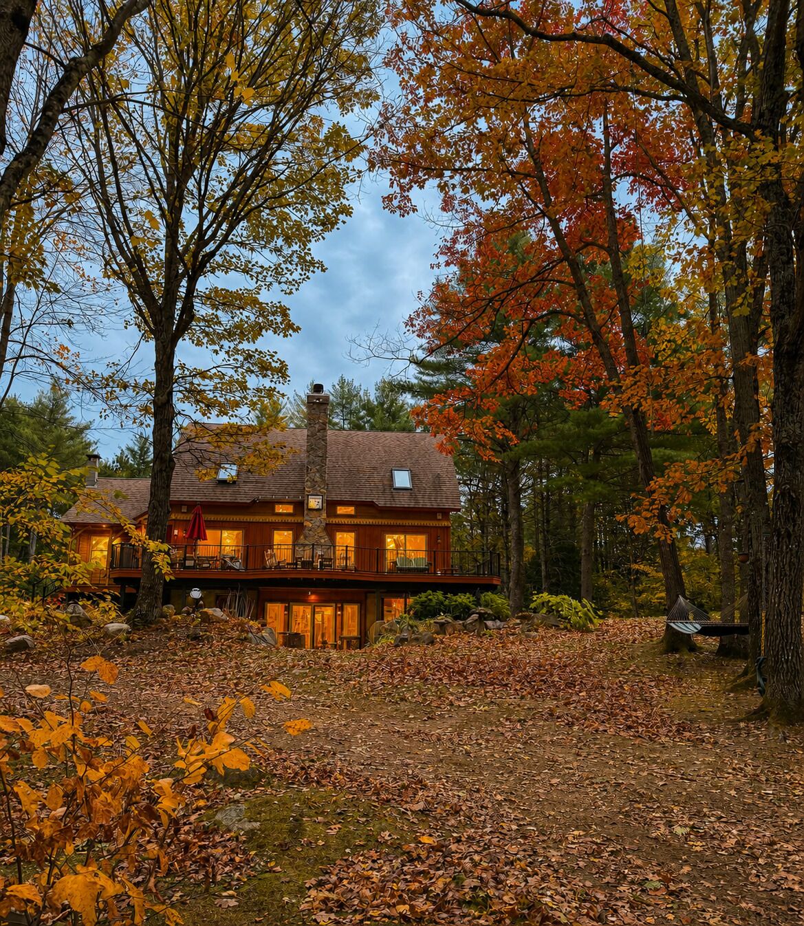 A two-story log cabin with a balcony, surrounded by autumn foliage.