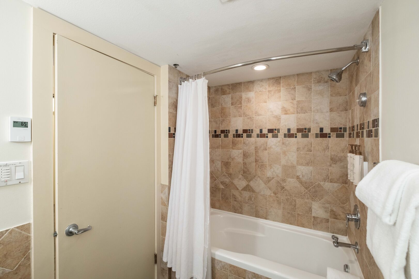 A bathroom with a bathtub, shower, and a door with a thermostat.