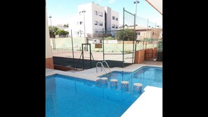 Une piscine avec des marches permettant d’y accéder, entourée d’une clôture et avec des bâtiments en arrière-plan.