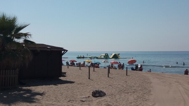 Une plage avec un abri en bois, des parasols et des gens qui se baignent.