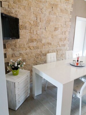 A modern dining area with a stone wall, a white table, and a TV mounted on the wall.